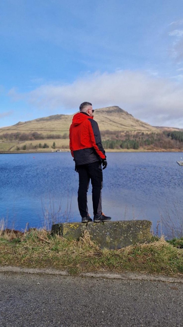 A walker in a red jacket beside a reservoir with hills behind